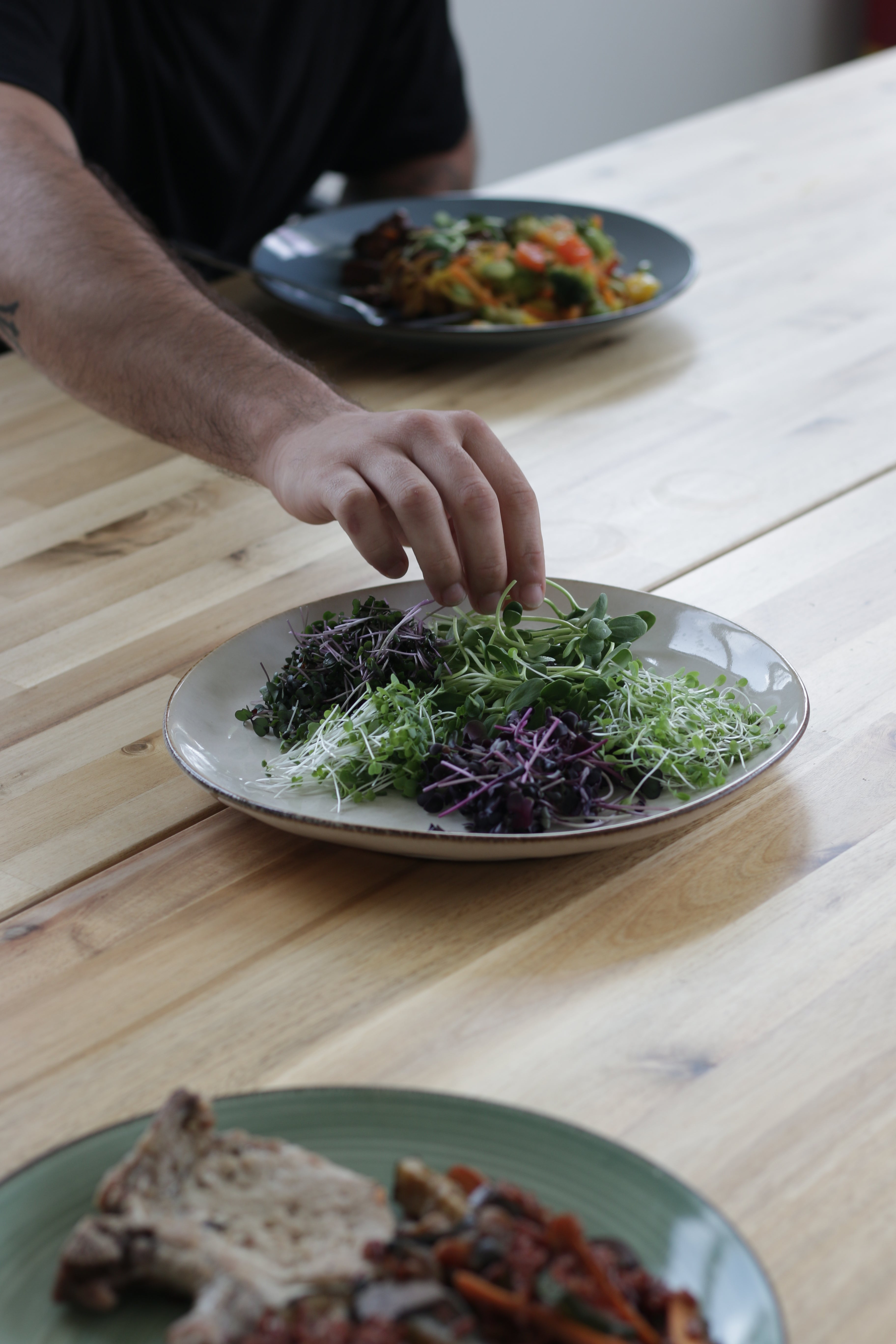 Person preparing a salad with various greens on a wooden table
