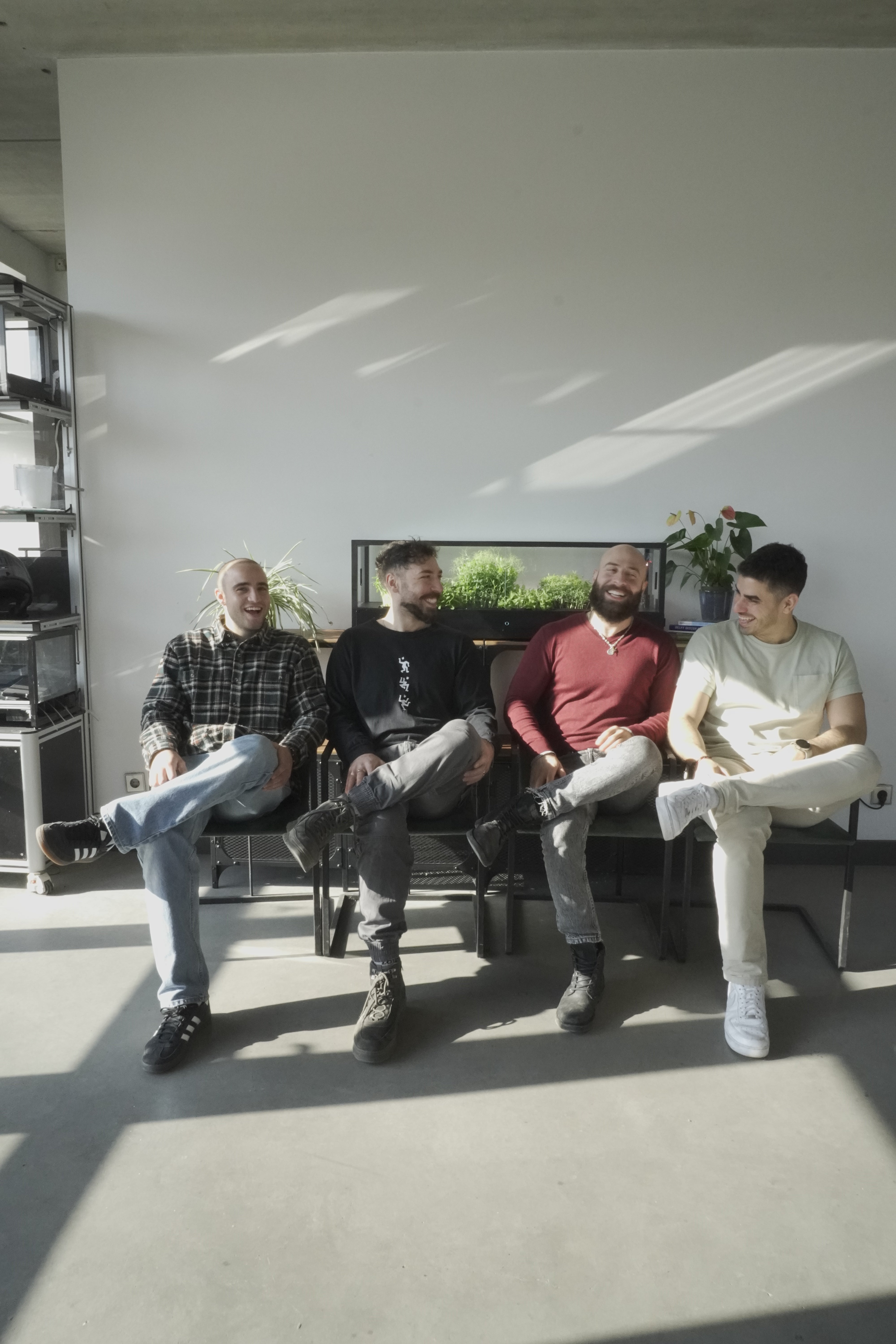 Four men sitting on chairs in a modern office with sunlight streaming in, with an indoor microfarm in the back.