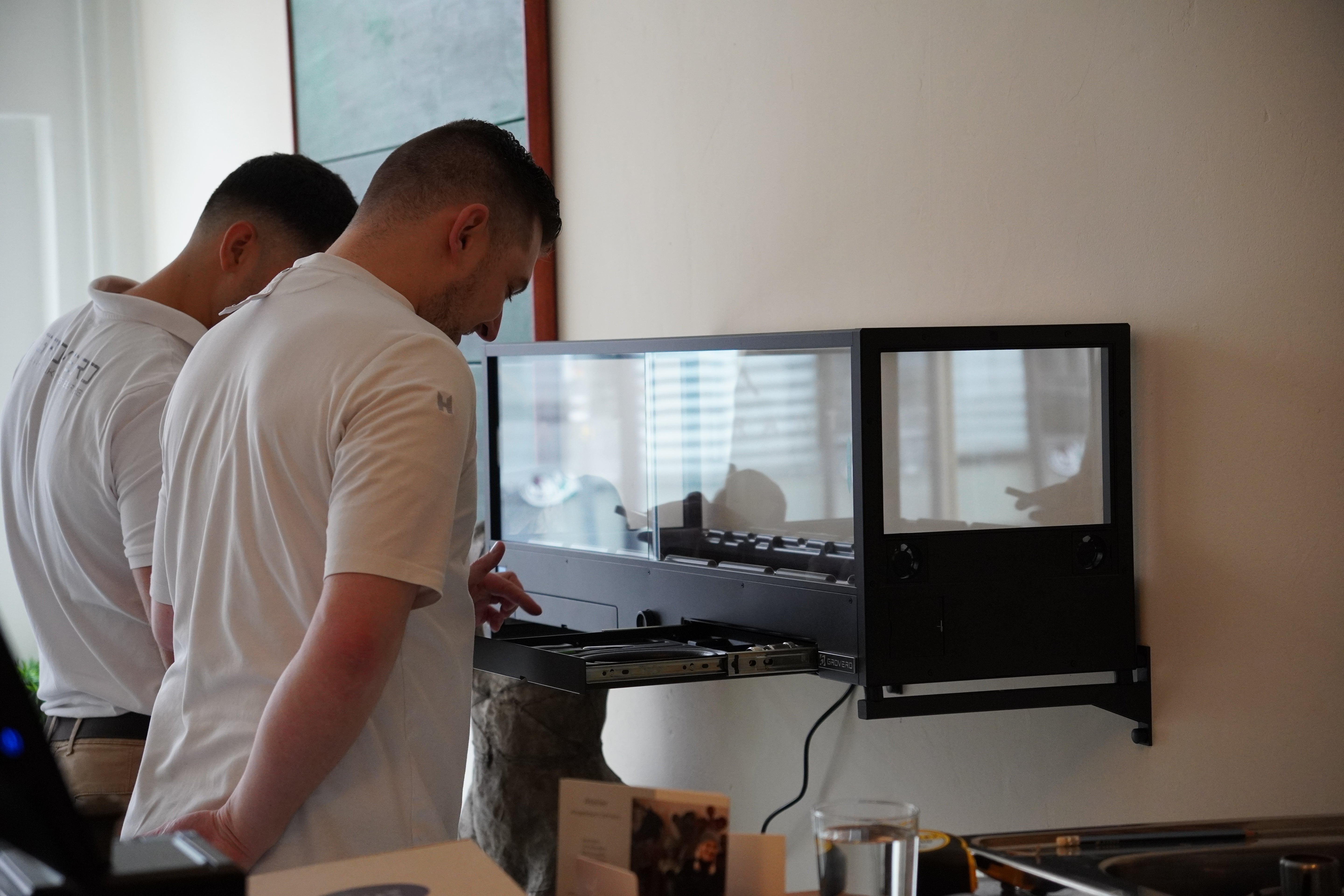 Two chefs standing in front of an indoor microfarm, inspecting its accessories.