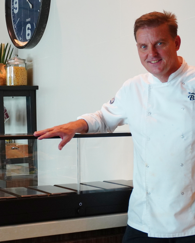 Man in a chef's coat standing in front of an indoor microfarm.