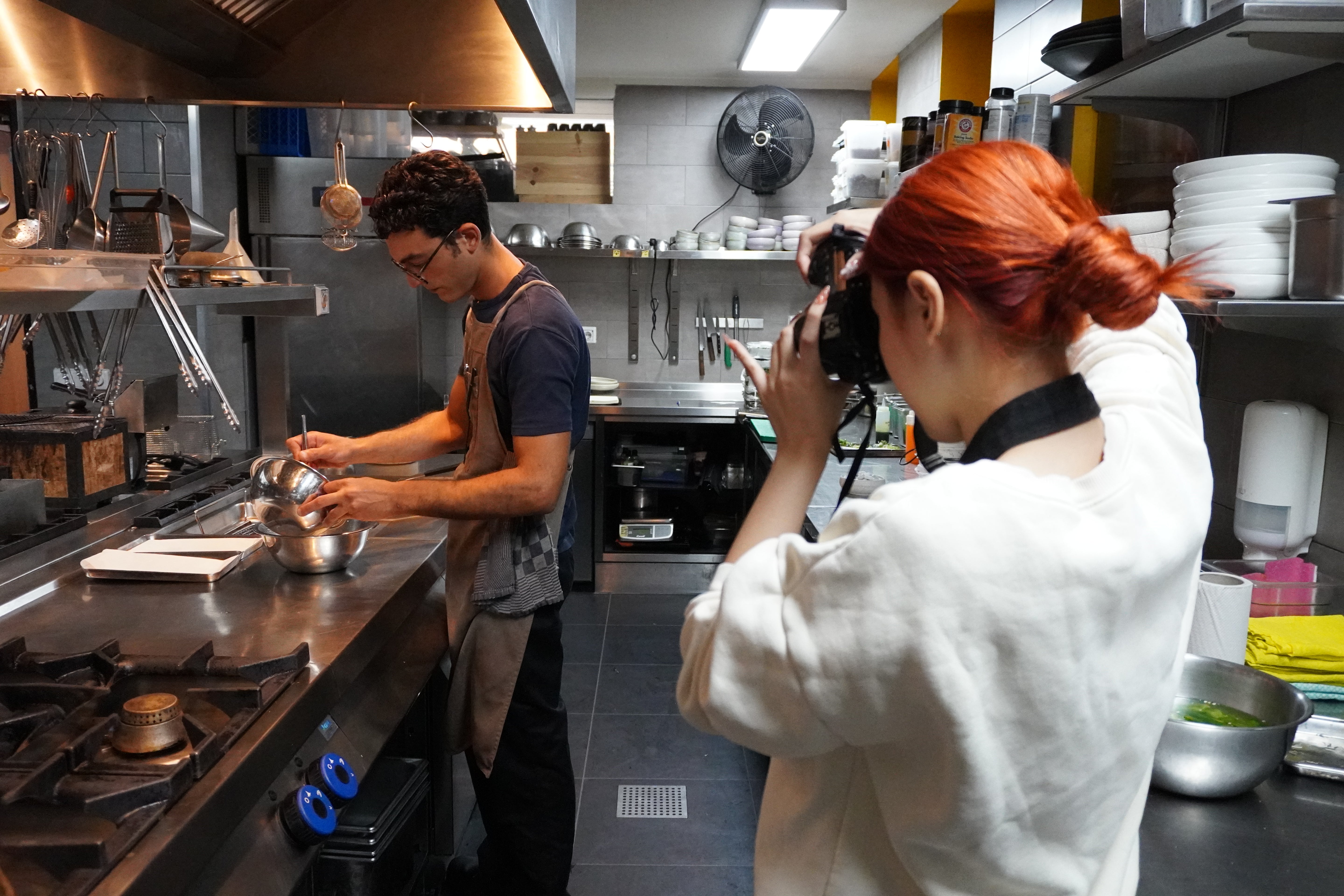 Two people in a kitchen, one taking a photo of the other.