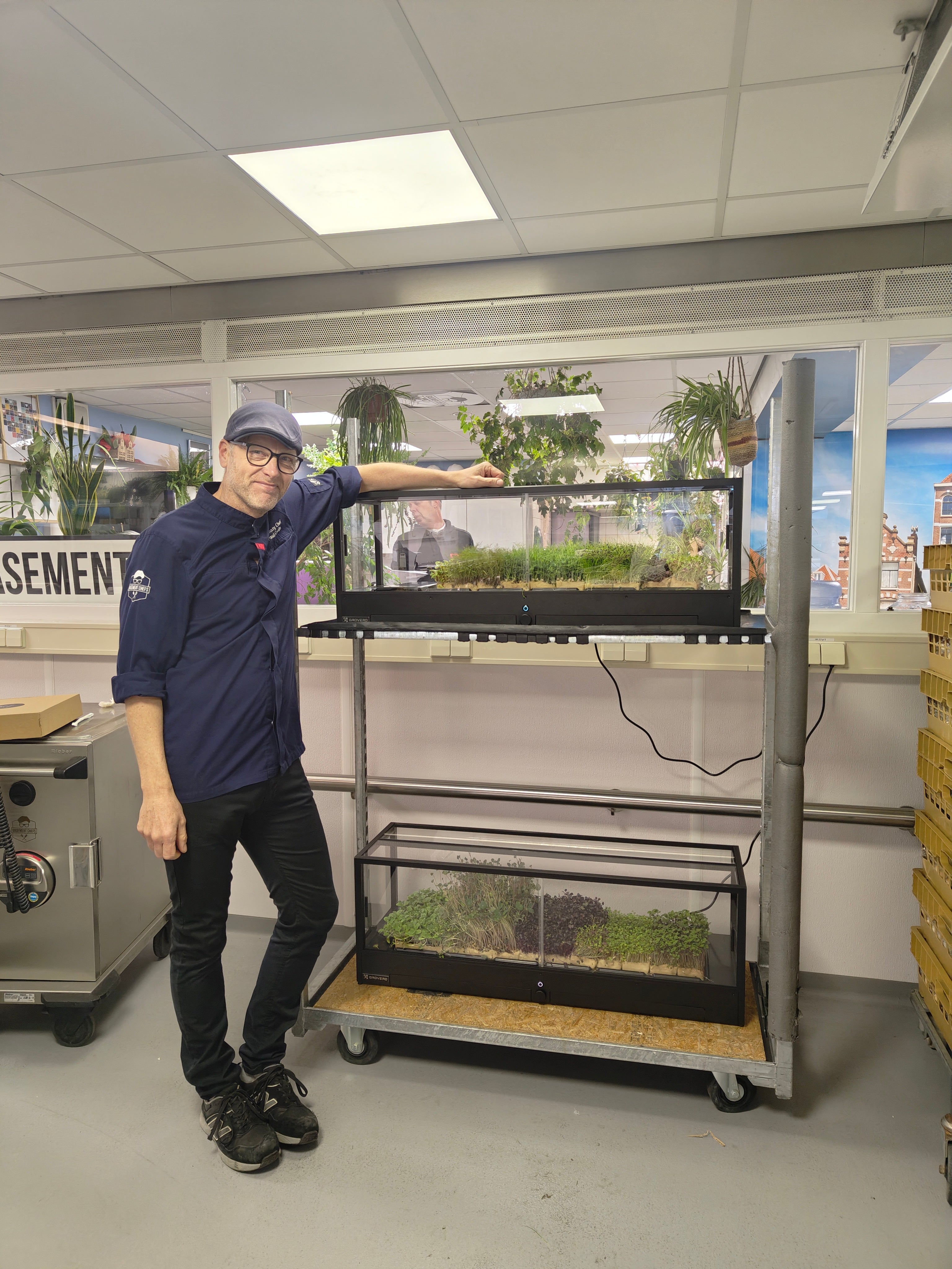 Chef standing in front of an indoor microfarm, with green growing inside.