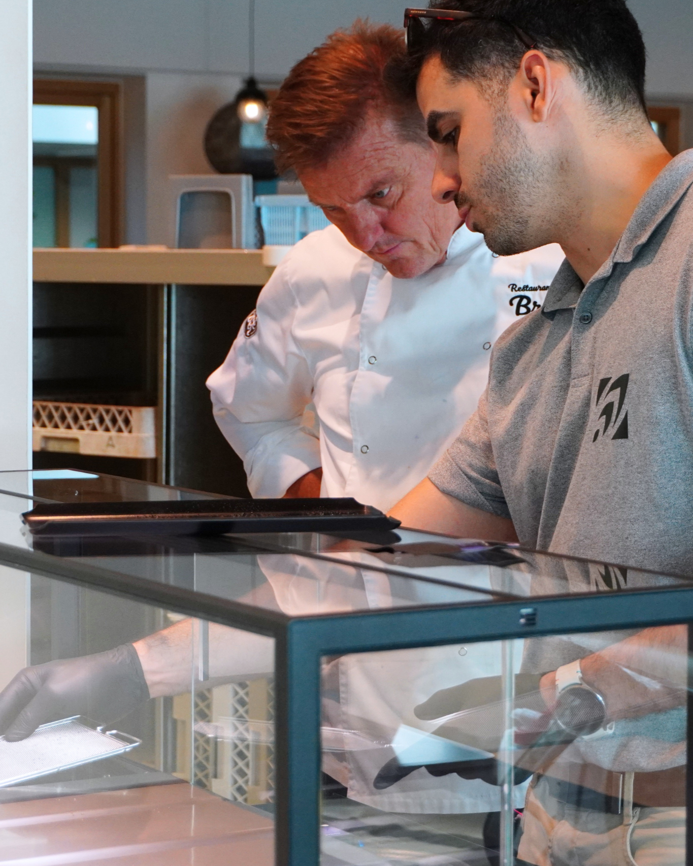 Two individuals, one in a chef's uniform, looking at an indoor microfarm in a kitchen setting.